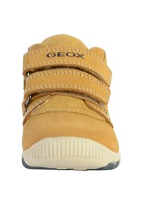 Zapatilla de cuero marrón con dos correas de velcro, parte superior texturizada, suela de goma y puntera reforzada. Nombre de la marca "GEOX" destacado.