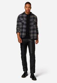 Karierter Flanellhemd in Grau und Schwarz, schwarzes T-Shirt, schlanke schwarze Lederhose mit seitlichen Schnürungen und schwarze Knöchelstiefel.