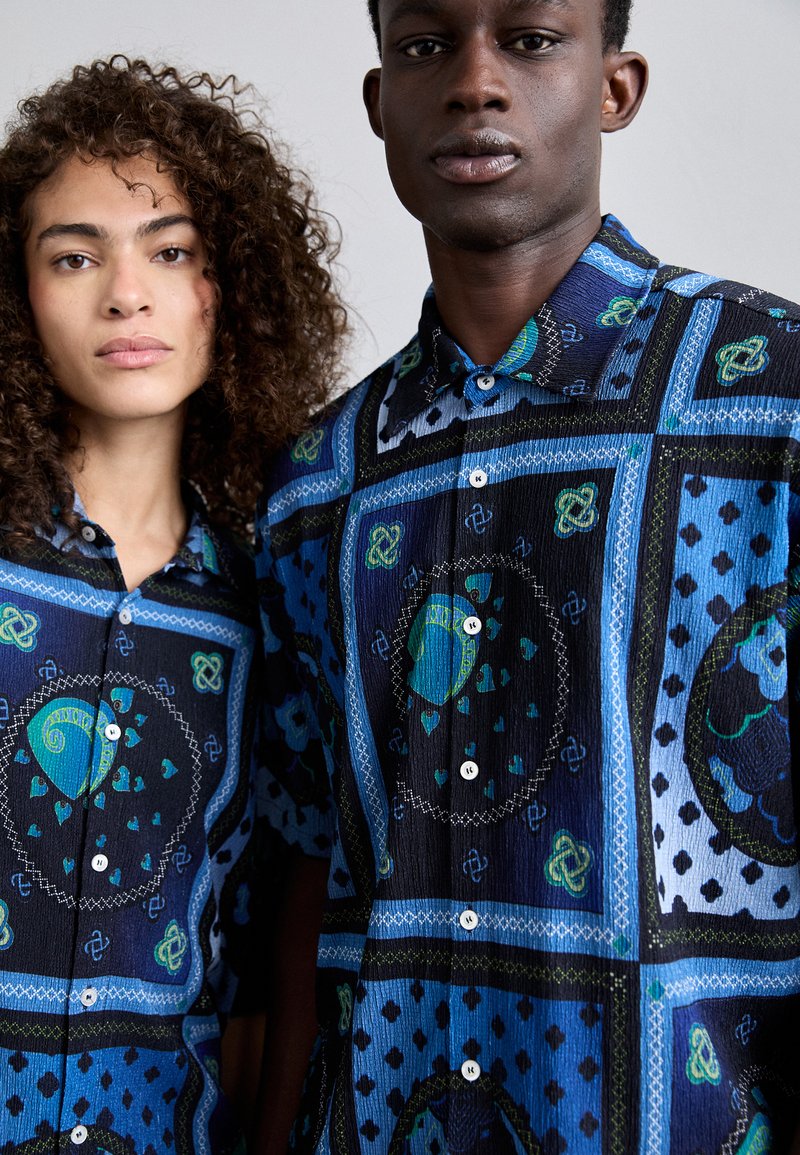 Chemises à boutons en tissu texturé, présentant des motifs en bleu, noir et vert. Détails notables : boutons ronds, cols bandeaux.