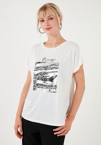 Hvid t-shirt med kortærmer lavet af letvægtsstof, med et sort og sølv grafisk print foran med abstrakte mønstre.