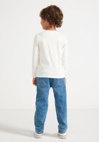Witte langemouwen shirt met een ribbelstructuur, gecombineerd met blauwe denim jeans. De jeans hebben een traditionele vijf-pocket ontwerp.