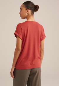 Haut courte en rouge rouille avec un motif en diamant texturé, présentant un col rond et des manches retroussées. Tissu lisse avec une coupe décontractée.