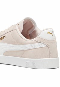 Baskets Puma en daim rose clair avec semelle blanche, bande latérale blanche et logo Puma doré sur le talon et le côté.