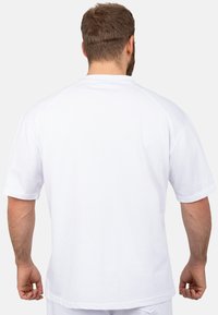Camicia bianca a maniche corte realizzata in tessuto leggero, con scollo rotondo e maniche raglan. Texture liscia, design minimale, senza motivi.