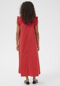 Červené maxi šaty z bavlny s krátkymi volánovými rukávmi, rovného strihu a jednofarebné. Čierne ploché topánky dopĺňajú outfit.