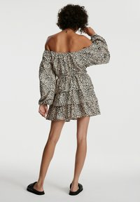 Leopardenmuster-Kleid mit schulterfreiem Design, gerafftem Taillenbund, langen, lockeren Ärmeln und mehrlagigem Rüschensaum. Strukturierter, leichter Stoff.