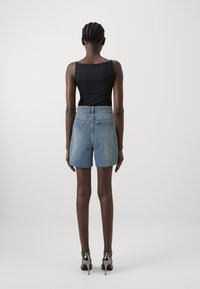 Zwarte mouwloze top gecombineerd met lichtblauwe denimshorts. De shorts hebben een hoge taille, een rafelige zoom en achterzakken. Het model draagt zilveren hakken.