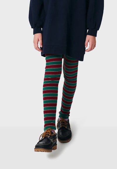 Leggings rayés verts et rouges avec une texture côtelée, associés à des chaussures noires et un haut oversized bleu marine, mettant en valeur des couleurs de vacances ludiques.