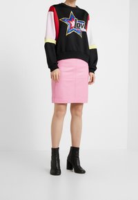 Mustapaita, jossa on värikäs tähtikuvio, vaaleanpunainen lyijykynähame ja mustat korkokengät nilkkaan. Paidassa on paljetit ja rohkeaa tekstiä.