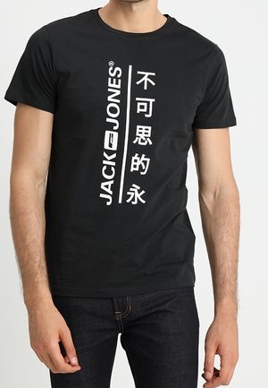 Mężczyzna ubrany w czarny T-shirt z krótkim rękawem, z białym pionowym napisem „JACK & JONES” oraz chińskimi znakami z przodu.