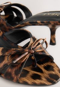 Sandales à talons imprimé léopard avec une semelle en cuir noir, bout ouvert, et détail de nœud décoratif. Elles disposent de fines brides et d'un talon fin.