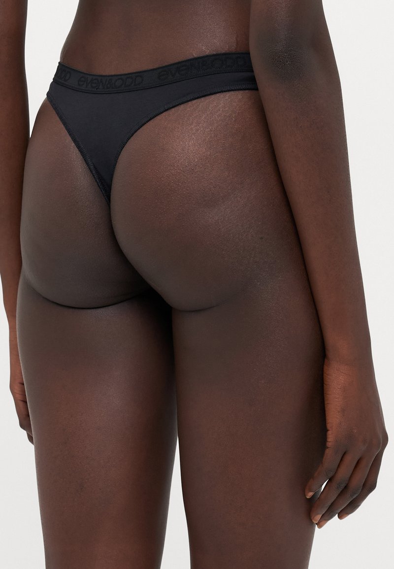 String noir en tissu doux, avec des côtés étroits et une ceinture élastique portant le logo "even&odd".