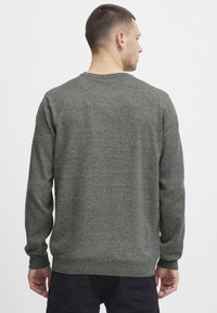 Sudadera de punto de color verde oscuro, cuello redondo, mangas largas, puños y dobladillo acanalados, tejido texturizado con un sutil patrón jaspeado.