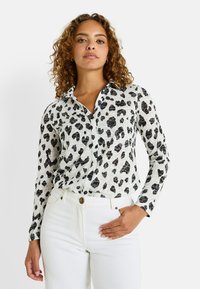 Chemise blanche à manches longues avec imprimé léopard noir, boutonnée à l'avant et avec un col, assortie à un pantalon blanc taille haute.