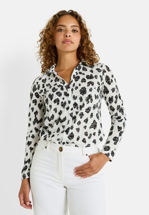 Chemise blanche à manches longues avec imprimé léopard noir, boutonnée à l'avant et avec un col, assortie à un pantalon blanc taille haute.