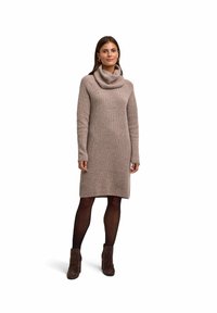 Vestito a maglia color marrone chiaro, con collo a cascata e maniche lunghe. Indossato con collant scuri e stivaletti alla caviglia. Tessuto liscio e strutturato.