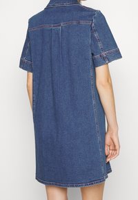 Denimklänning med korta ärmar, skräddarsydd krage, sidofickor och kontrasterande röd söm. Långt något löst sittande.