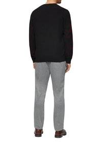 Zwarte trui met rood abstract patroon op de mouwen, gecombineerd met lichtgrijze joggingbroek. Stoffen lijken zacht met een relaxte pasvorm.