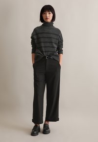 Dunkelgrauer gestreifter Rollkragenpullover, kombiniert mit hochgeschnittenen schwarzen Hosen und klobigen schwarzen Loafers, schafft eine lässige Silhouette.