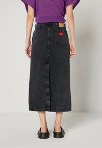 Svart denim-midi kjol med en mittendelning, som har en lappläck på framsidan och en design med röda läppar på baksidan, ihop med en lila topp.