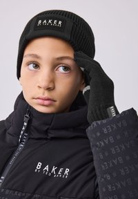 Black ribbed beanie with a label, black knit gloves with gray accents, and a padded jacket featuring repeated branding in dark shades.
