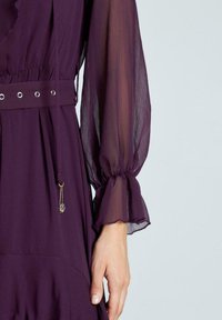 Vestido púrpura con mangas largas transparentes y puños elásticos, cintura ceñida con ojales metálicos y un cordón decorativo con una cuenta.