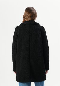 Black faux fur coat with a textured surface, a collar, long sleeves, and a straight silhouette, reaching mid-thigh in length.