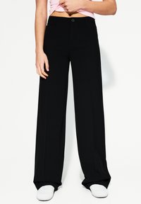 Pantalons larges noirs en tissu lisse, dotés d'une fermeture à bouton sur le devant et de deux poches latérales, associés à un top rose cropped.