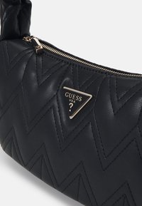 Borsa a mano in pelle nera con design trapuntato a zigzag, hardware dorato e logo triangolare sul davanti. Dotata di chiusura con zip.