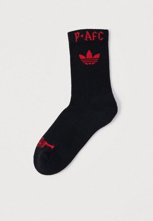 Črna bombažna nogavica z rdečim napisom "P*AFC" in rdečim logotipom Adidas s tremi črtami, rebrastim zaključkom in okrepljenim prstom.