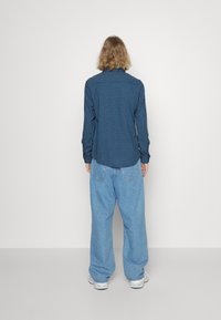 Langsleeve blauw geruite shirt met kraag, gedragen met losse lichtblauwe jeans, met een relaxte pasvorm en subtiele textuur.