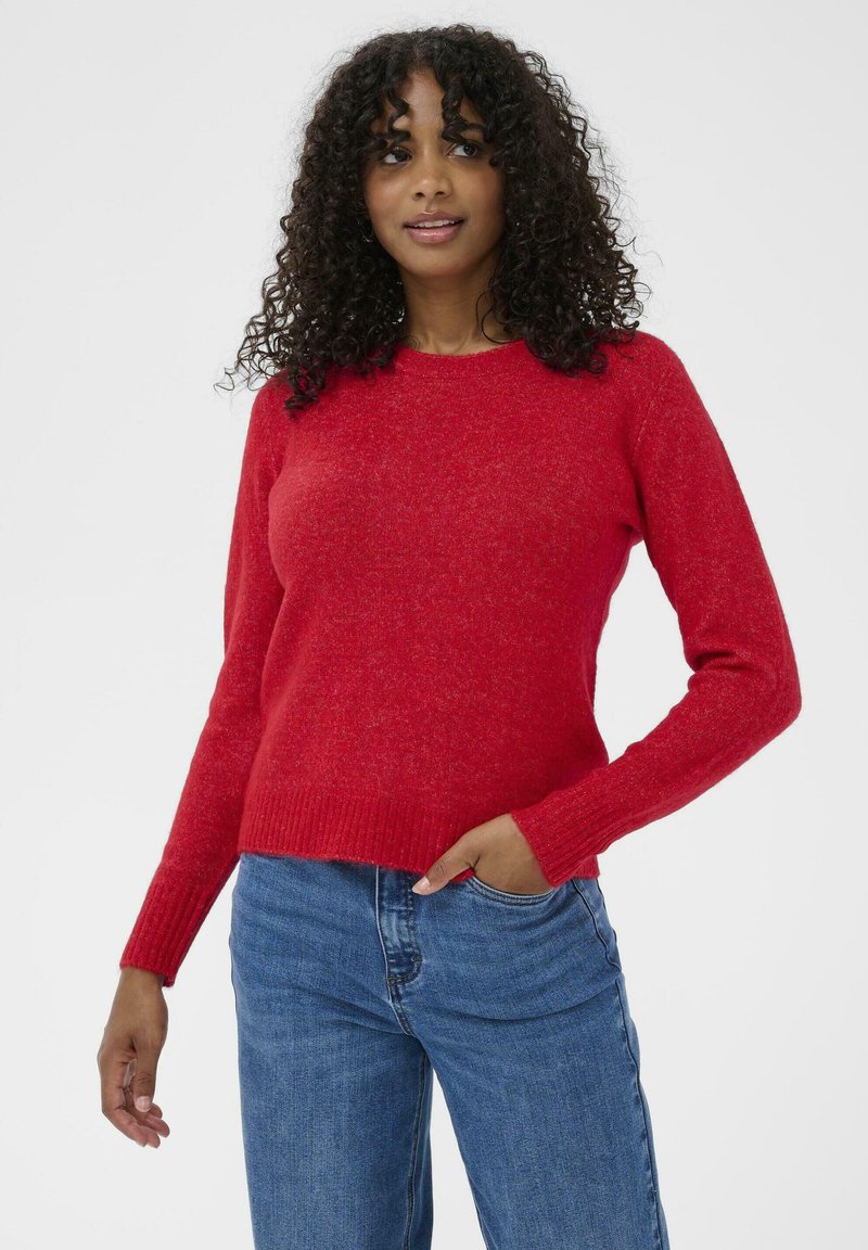 Pulover roșu dintr-un material texturat, cu mâneci lungi, manșete cu rimă și un tiv drept. Asortat cu blugi bleu din denim.