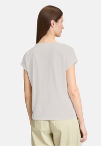 Lichtgrijs T-shirt met korte mouwen en opgerolde mouwen, ronde halslijn, zachte textuur en zijsamenvoegdetails, gedragen met lichte broek.