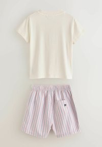 T-shirt à manches courtes blanc cassé associé à un short taille élastique à rayures verticales roses et bleues, avec un petit détail de poche arrière.