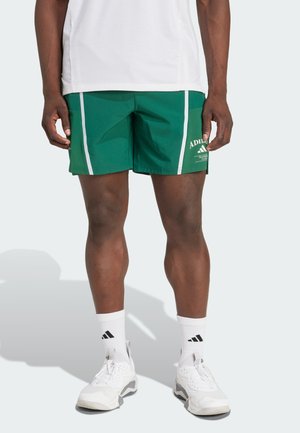 Žalios sportinės šortai, pagaminti iš lengvos medžiagos, su baltais šoninėmis juostelėmis, logotipu šone ir klasikinio sportinio dizaino.
