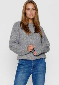 Grijze gebreide trui met een relaxte pasvorm, ribgebreide manchetten en een textuurstof, gecombineerd met blauwe denim jeans. Eenvoudig, casual ontwerp.