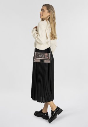 Umhängetasche mit einem bedruckten Design, das pastellfarbene Töne und Texturen aufweist, ergänzt durch einen Kettenriemen. Schwarzer Plissèrock und glänzende Schuhe.