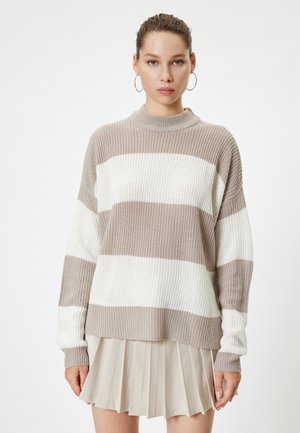 Beige ja valge triibuline kudum, millel on kõrge kaelus ja lõdvalt istuv lõige, koos pleeditud kreemja seeliku ja reljeefse kangaga, millel on soonikkoes mansetid.