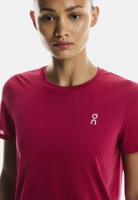 Prilagojena športna majica s kratkimi rokavi v živo roza barvi, izdelana iz tkanine, ki odvaja vlago. Ima majhen beli logotip na levem prsnem delu.