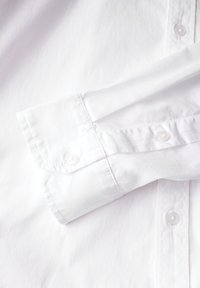 Camicia bianca con colletto rigido, in morbido cotone, e due bottoni sui polsini con cuciture di rinforzo.