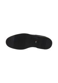 Semelle de chaussure noire avec une texture antidérapante et un petit détail du drapeau italien près de l'arche sur un fond blanc.