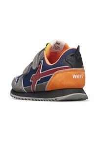 Sneaker con strap in velcro caratterizzato da suede grigio, tessuto blu navy, dettagli rossi e arancioni, e una suola nera texture con un logo distintivo sul retro.