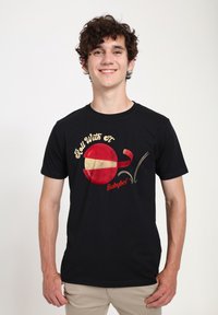 Sort T-shirt med et rødt og gult Babybel-oste grafik og teksten "Roll With It" i guld. Korte ærmer, lavet af bomuldsmateriale.