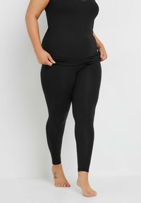 Svarta leggings tillverkade av elastiskt material, med en slät yta och en åtsittande design, ihop med en svart linne med spetsdetaljer.