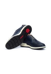 Chaussures en cuir texturé marine avec semelles blanches et accents rouges. Présentent un bout rond et un design à lacets, mettant en avant des motifs d'adhérence au fond.