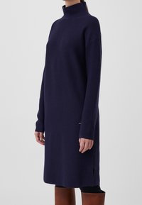 Robe-pull col roulé bleu marine avec manches longues, poignets côtelés, fentes latérales et un accent métallique près de l'ourlet. Confectionnée en tissu tricoté doux.