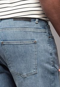 Jeans de denim azul claro con corte recto, que presentan dos bolsillos traseros, costuras sutiles y una etiqueta de cuero en la cintura.