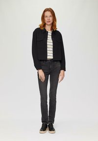 Zwarte cropped jacket met twee voorkruiden over een wit en gestreept shirt, gecombineerd met donkere skinny jeans en zwarte sneakers.