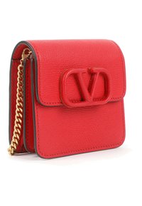 Pequeño bolso de cuero texturizado rojo con una correa de cadena dorada y un logo "V" en relieve en la solapa frontal.