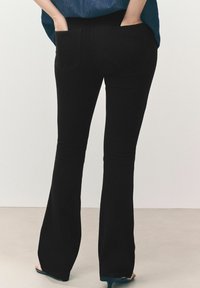 Pantaloni neri a zampa d'elefante con due tasche posteriori. Il materiale sembra liscio con una leggera lucentezza. La vita è alta e le gambe si allargano dal ginocchio.